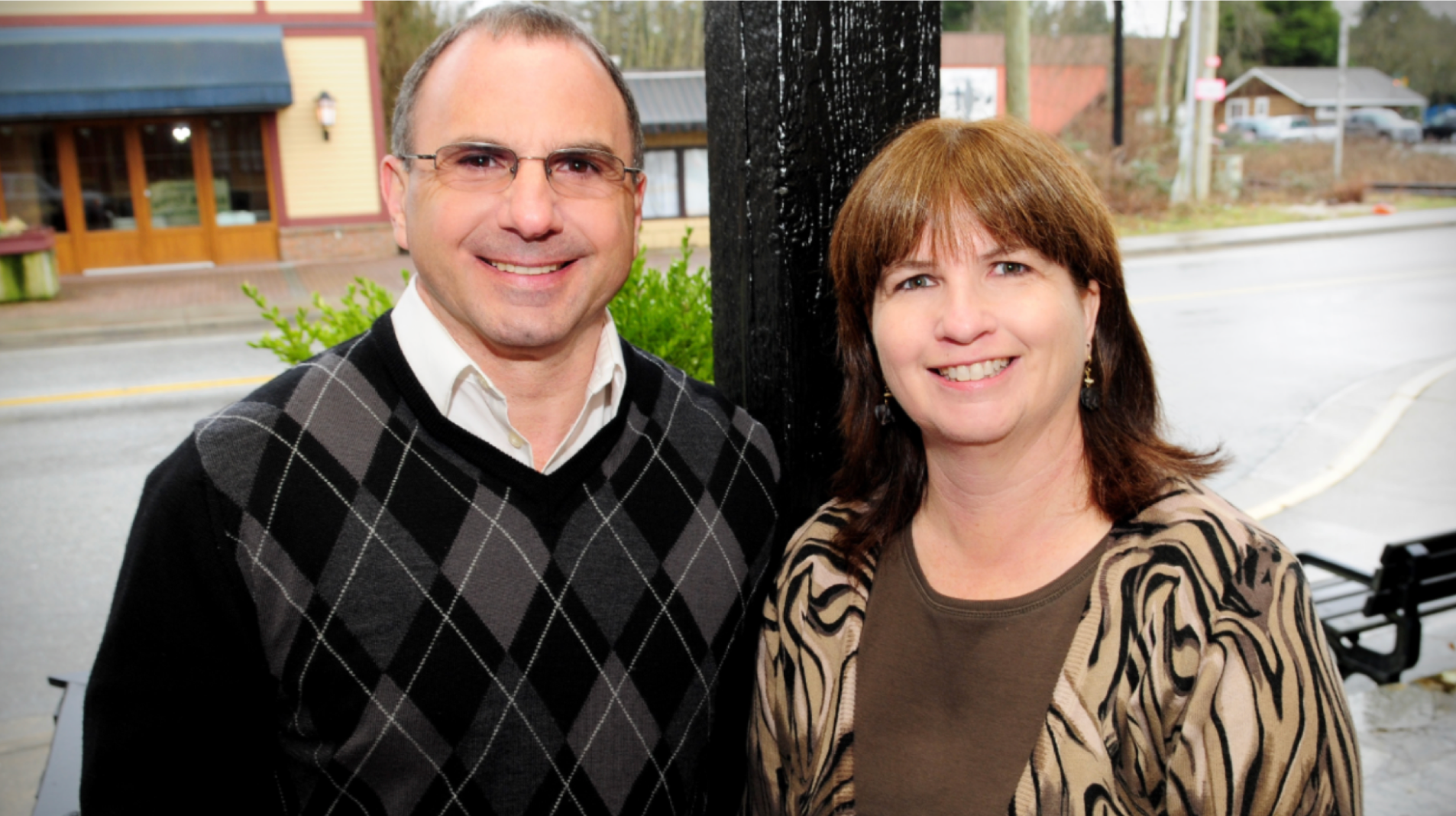 photo of couple smiling at camera behind a view of a street.