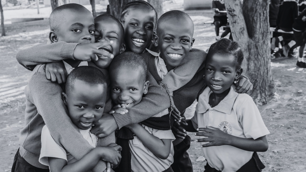 black and white photo of seven young school children hugging and smiling at camera