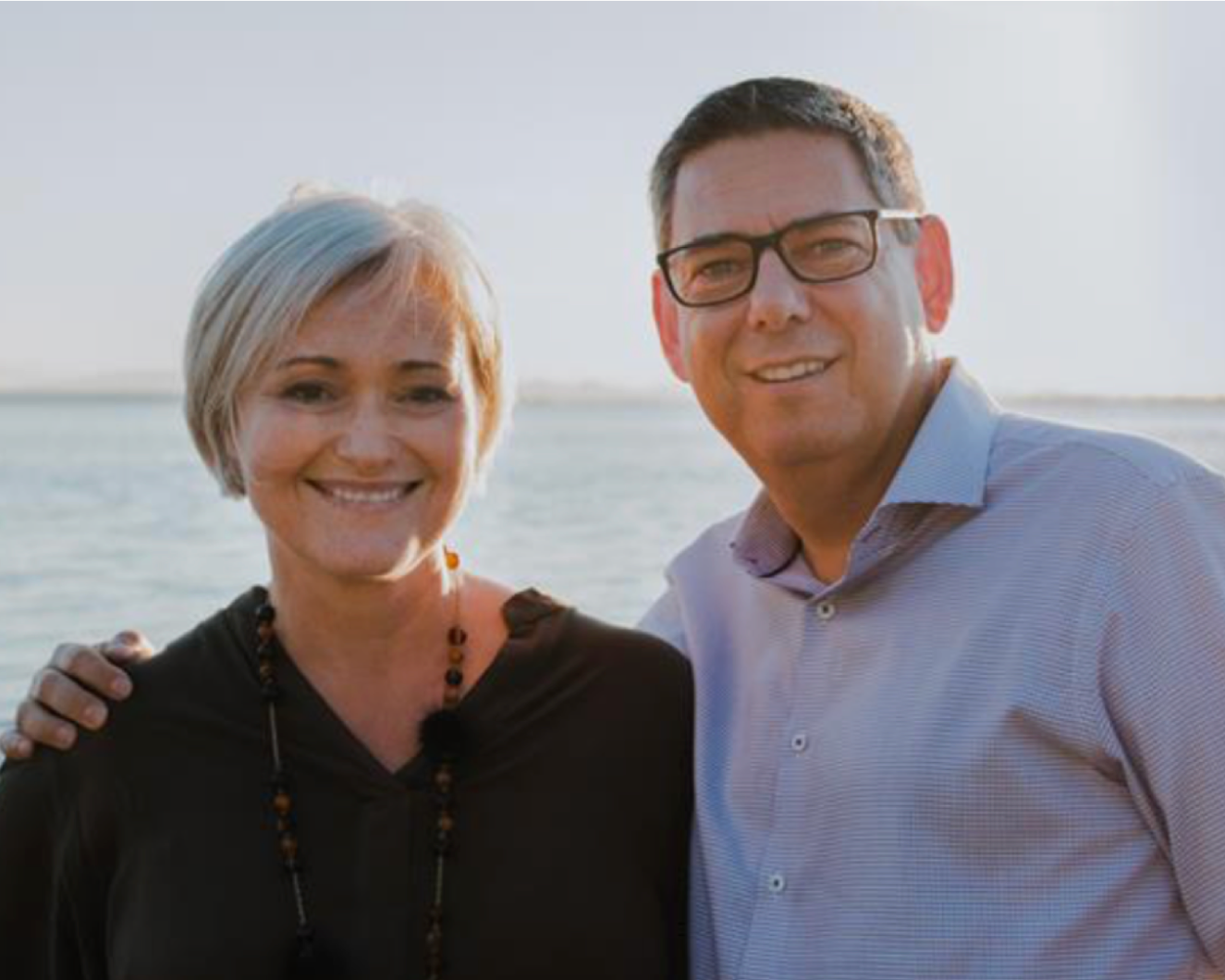 photo of couple smiling at camera behind view of a lake