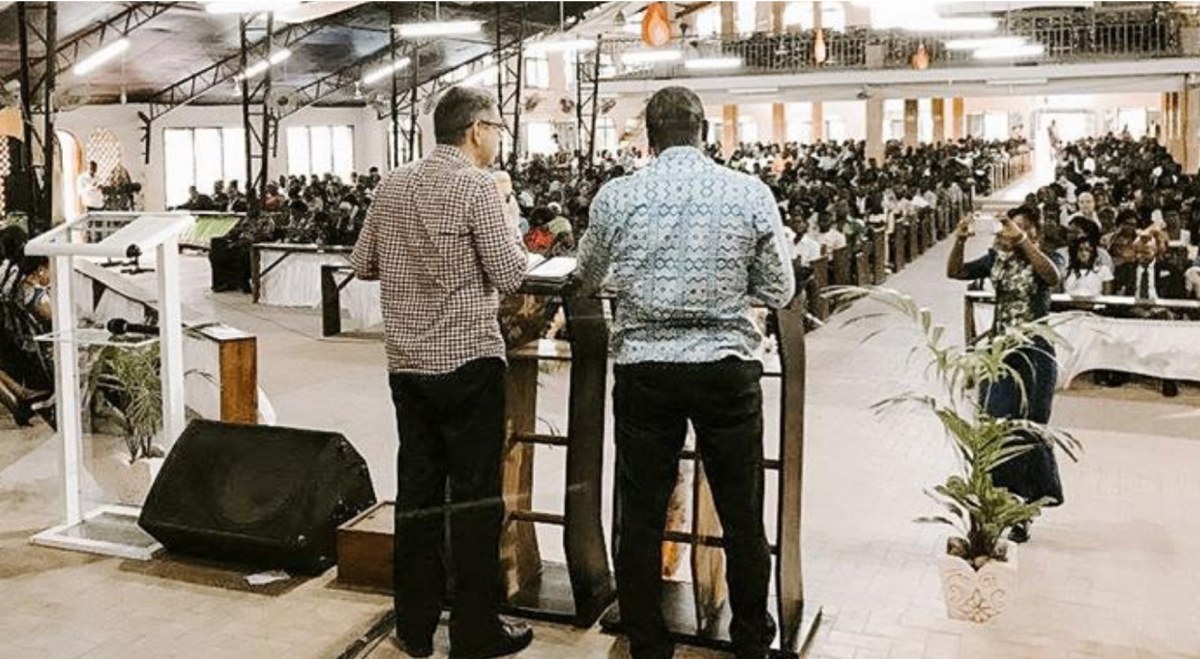 photo of two men at a pulpit speaking to a room full of people