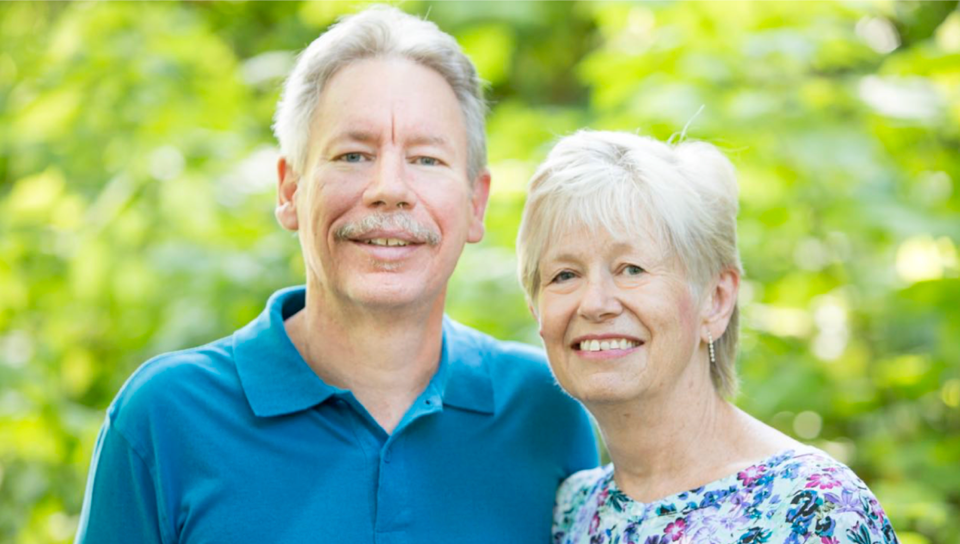 couple smiling at camera behind greenery