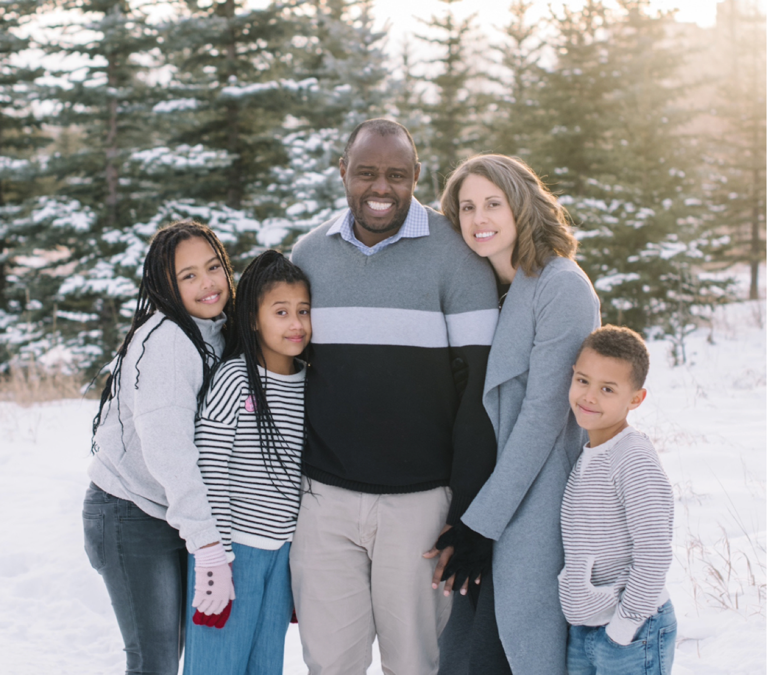 photo of couple and three young children smiling at camera behind scenery of snow and trees.