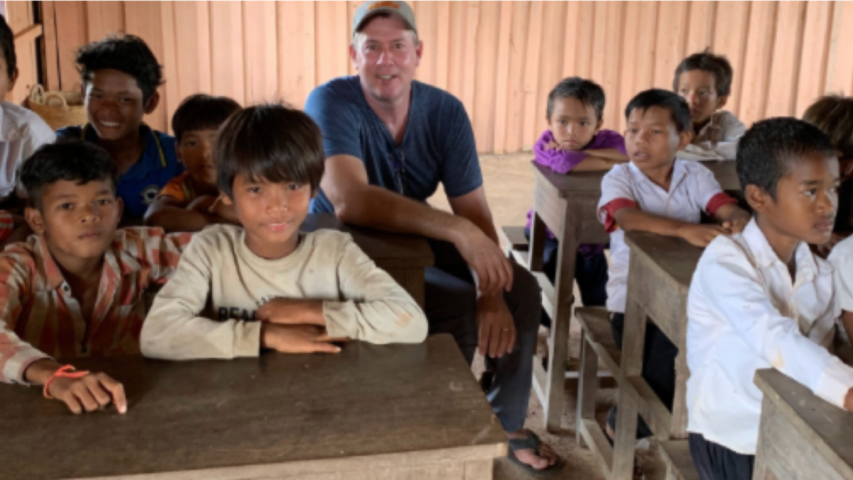 photo of students in classroom desks and man smiling at camera