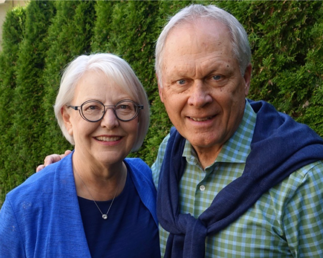 couple smiling at camera behind green scenery.
