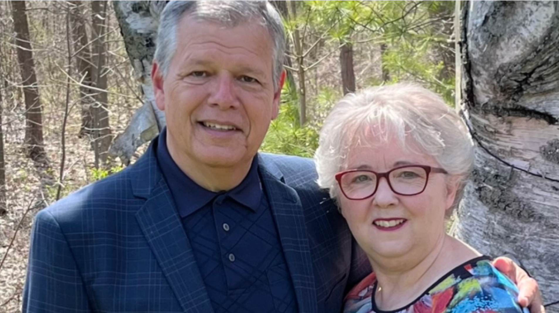 couple smiling at camera behind greenery and trees