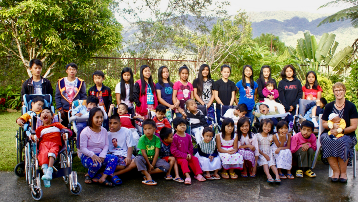 photo of GW and young children in a group photo behind green trees.